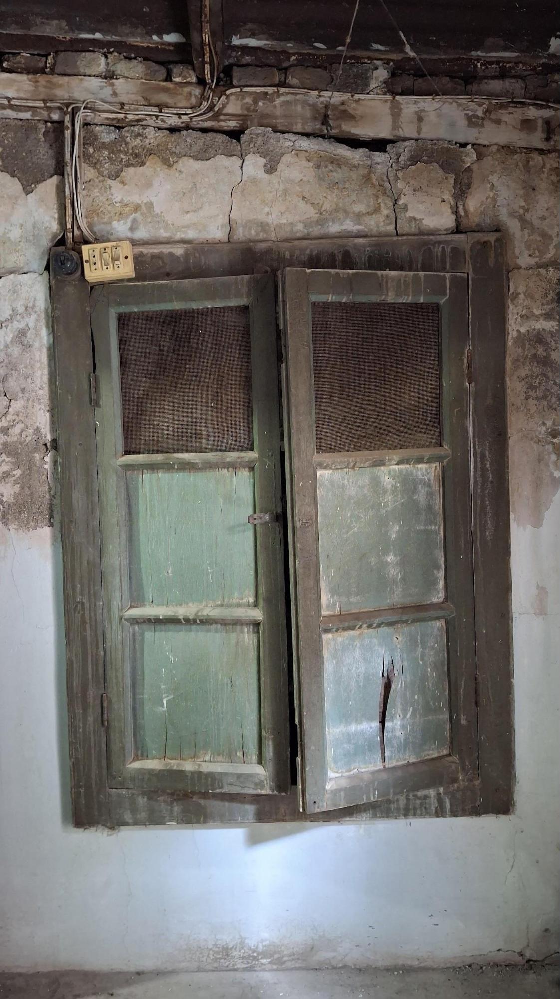A two-panel window with green panes in a worn wooden frame. The netted panel may be a more recent feature, added for ventilation. (Source: CKA Archives)