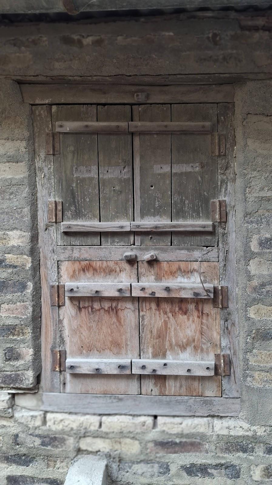 Three traditional windows which can be found across different corners of the house. This window reveals a weathered wooden design with horizontal planks set in a stone wall. (Source: CKA Archives)