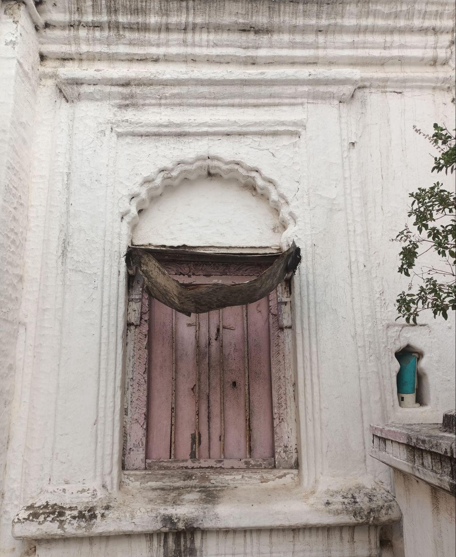The small windows that adorn the walls of the home vary in design. This window is framed by an elegant arch and has a wooden double-door design. (Source: CKA Archives)