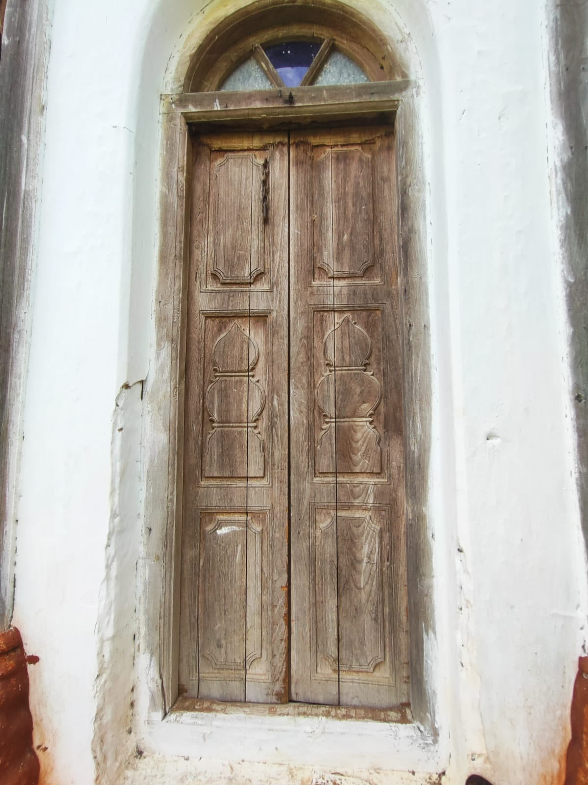 An elongated wooden door panel of the Wada which showcases sheds light on the early 20th-century carpentry techniques. The door has rectangular panels with recessed details, set within a plastered archway. The top and bottom panels feature geometric designs, while the middle panel includes a carved motif, possibly a kalash, used in religious rituals. (Source: CKA Archives)