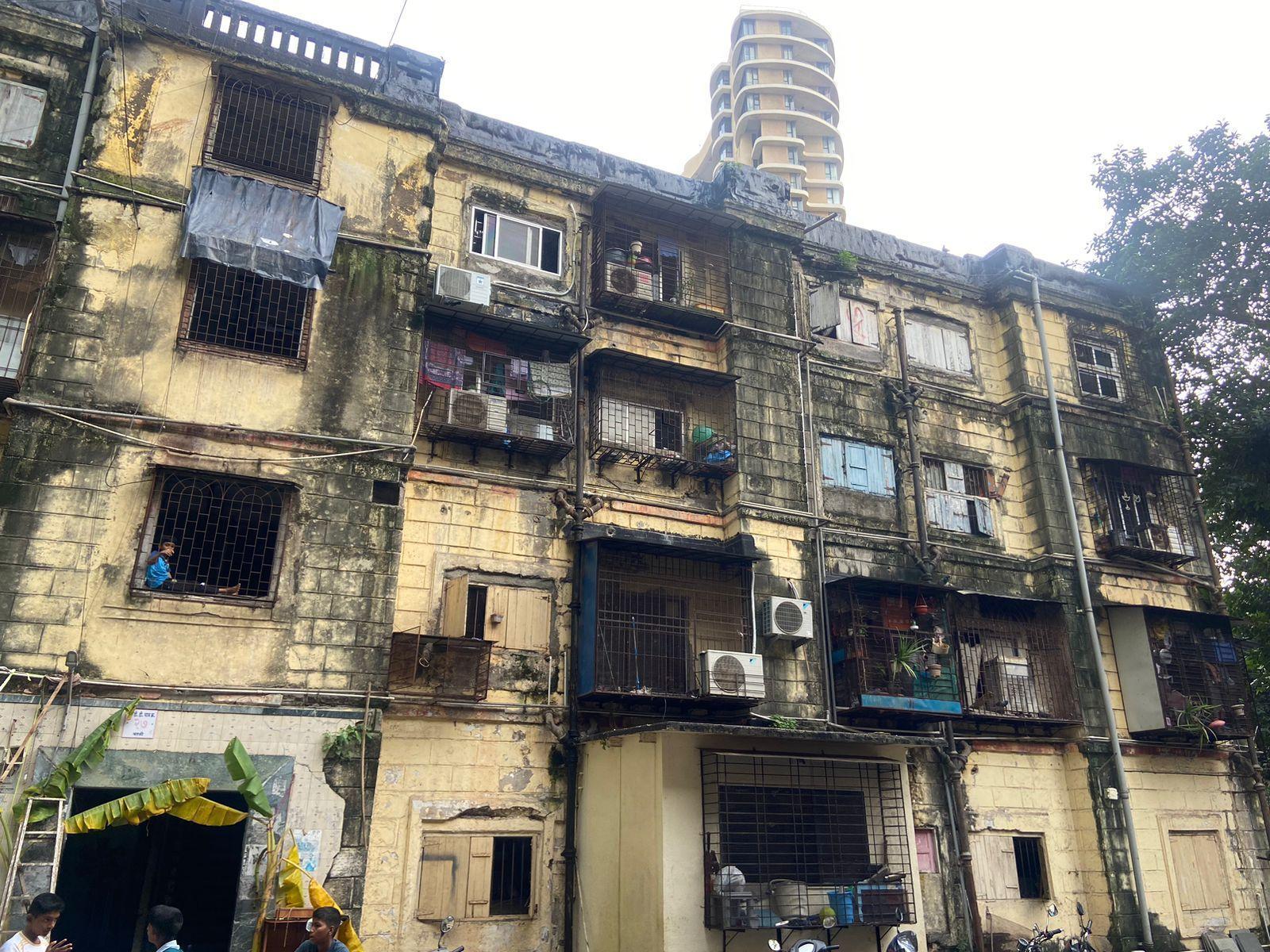 A four-storey structure with brick-textured embossing, neutral tones, and precast baluster parapets, featuring exposed drainage pipes and box window extensions. Source: CKA Archives
