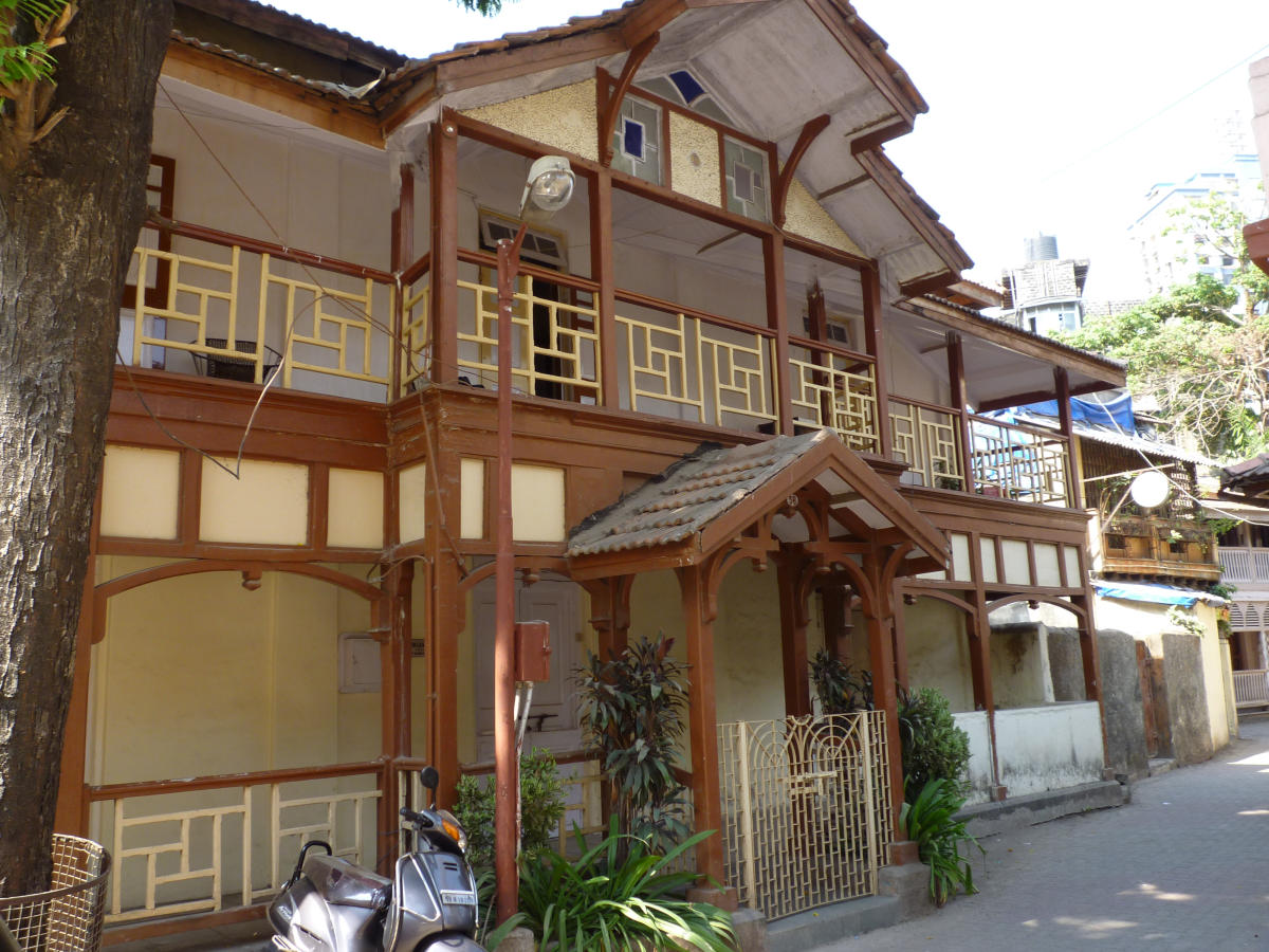 Brown and cream-colored timber house in Khotachiwadi with a wide front verandah and a projecting balcony overlooking the street. A sloping roof extends across the structure, including above the front porch.[20]