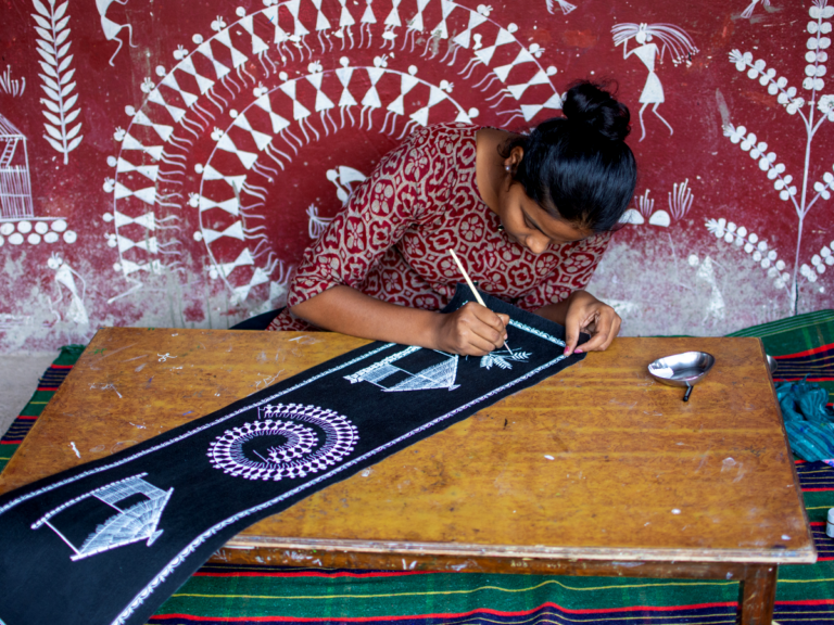 A woman creating traditional Warli art, showcasing the intricate indigenous painting style that reflects the rich cultural heritage of Palghar district.[5]