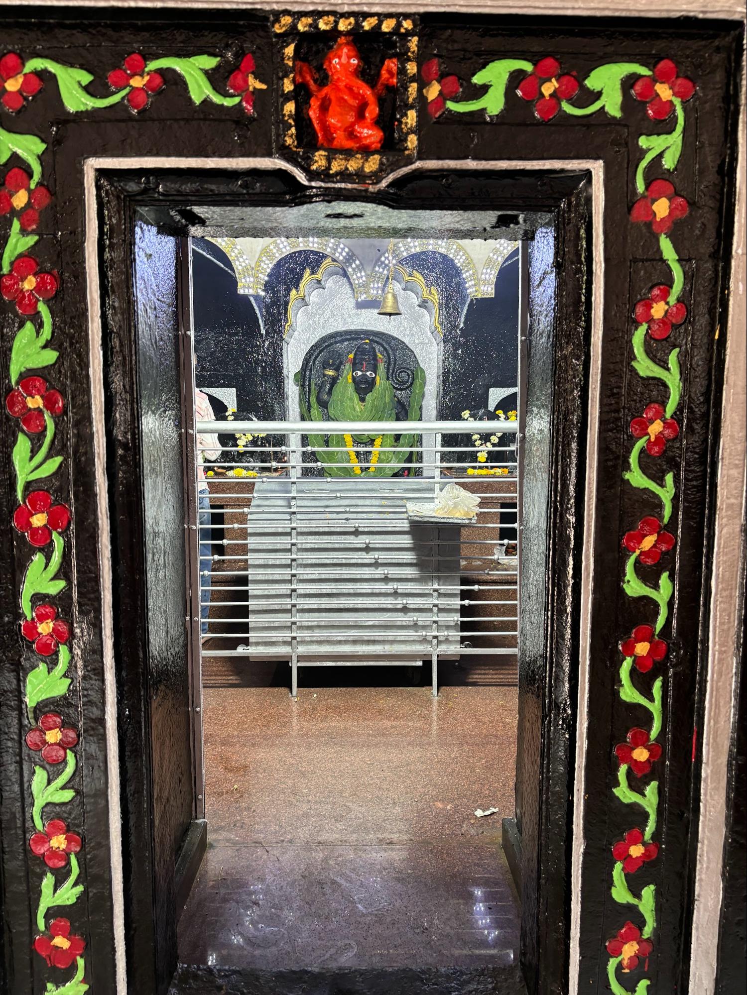The depiction of Bhagwan Maruti at the Dulya Maruti Mandir, Ganesh Peth, coated in vermillion, with wide, unblinking white eyes said to have once swayed. A portrait of Bhagwan Vitthal is placed at the threshold of the sanctum, watching over the space with quiet presence. (Source: CKA Archives)