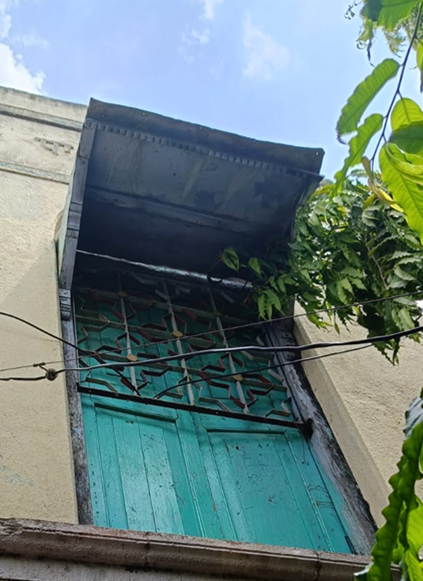 The window is painted a bright green color and has intricate floral grills. The Chajja seems to be constructed out of metal sheets and a wooden structure. (Source: CKA Archives)