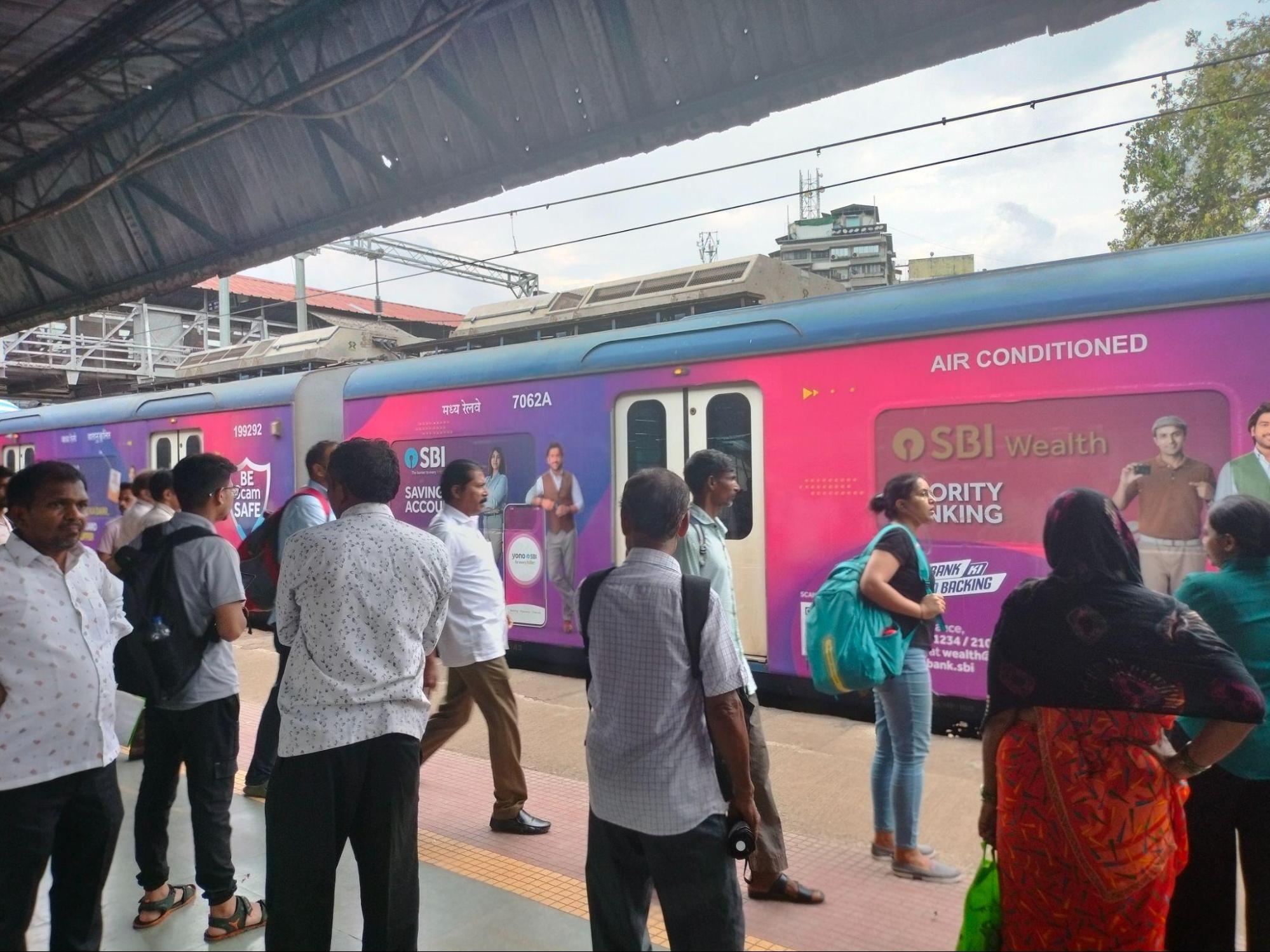 Commuters wait beside a newer air-conditioned Mumbai local train, branded with commercial advertisements. (Source: CKA Archives)