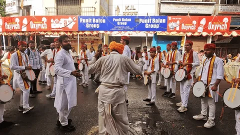 A Dhol Tasha Pathak performing during Ganpati, framed by layers of numerous commercial hoardings.